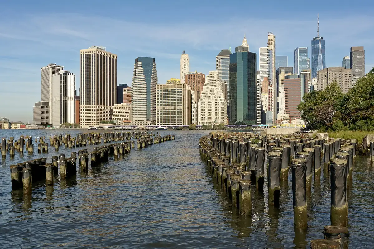Lower Manhattan skyline seen across the East River from Brooklyn Bridge Park, with old pier pilings in the water