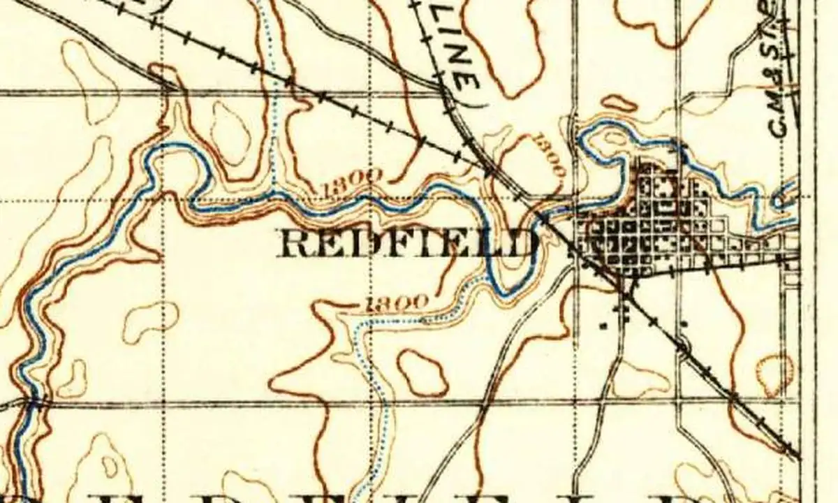 Detail of an 1899 U.S. Geological Survey map showing the street grid of Redfield beside a winding river, with two railroad lines crossing at the edge of town